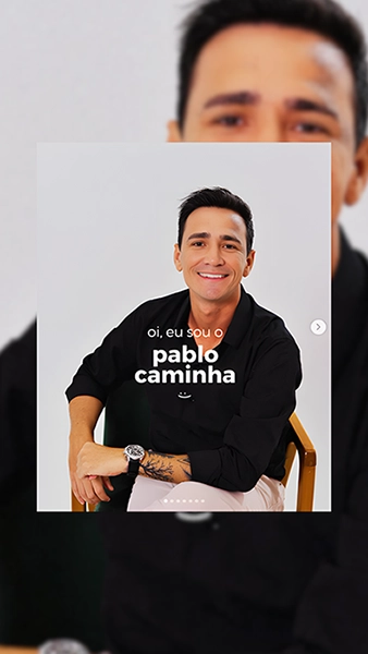 foto do Pablo, de camisa preta, sentado em uma cadeira com braço de madeira, sorrindo